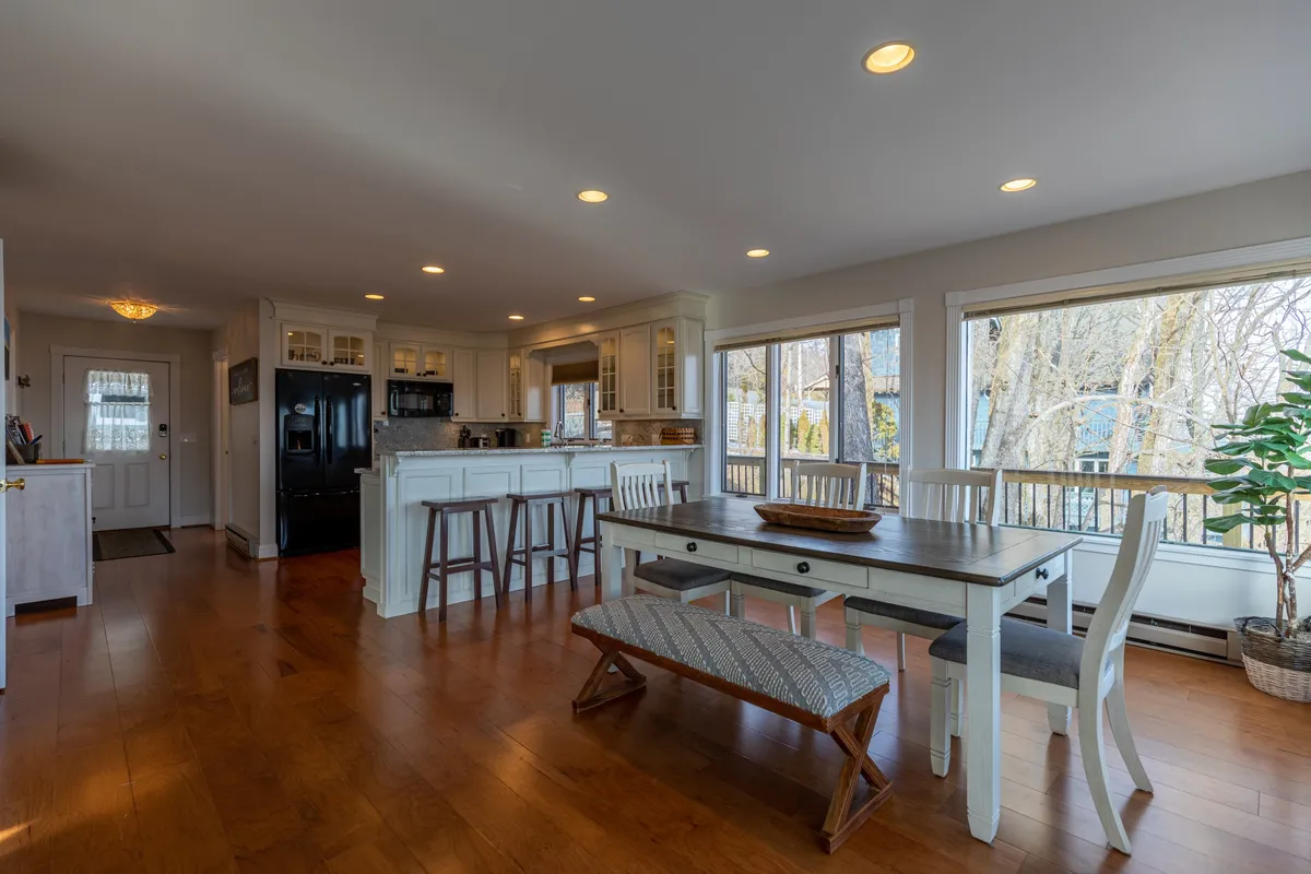 A welcoming dining area with a large wooden table, comfortable chairs, bright windows, and a kitchen island with sleek black appliances. The space exudes warmth, making it perfect for group dinners and relaxed mornings with a view.