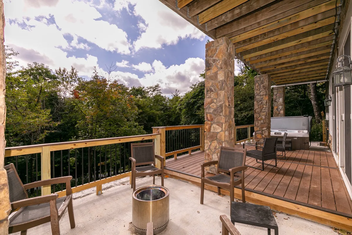A spacious wooden deck with stone pillars, a cozy fire pit, a spa area, and lush greenery—perfect for social gatherings, stargazing, or relaxing after a day of hiking. The inviting outdoor setup blends comfort with the natural mountain environment.