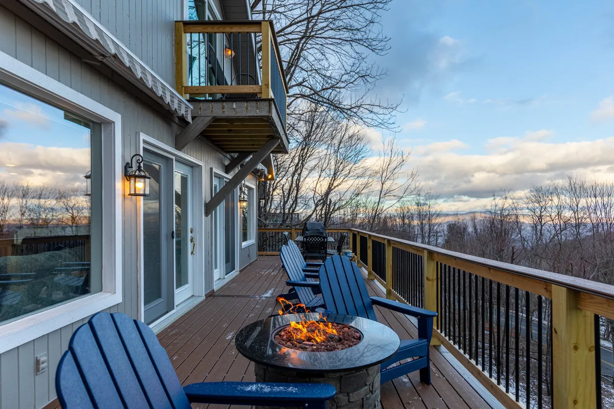 An outdoor fire pit area with Adirondack chairs arranged on a deck, overlooking sweeping mountain vistas. The scene suggests gatherings at sunset, with plenty of space for friends, family, and even pets to enjoy the view, share stories, or stargaze in the crisp evening air.