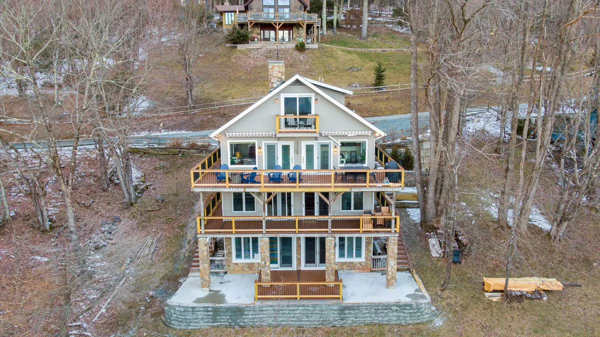 This exterior image showcases a striking three-story mountain home with multiple balconies, a stone facade, and lush trees surrounding the property. The balconies promise stunning vantage points for sunset viewing and enjoying fresh mountain air. The scene exudes tranquility and the inviting promise of outdoor relaxation.