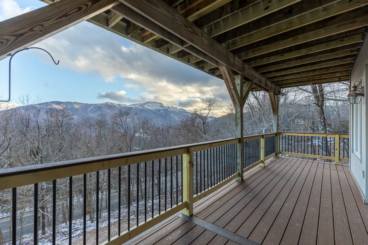 A wide-angle view of a wooden deck with classic railing, elevated to provide sweeping mountain vistas. The scene is peaceful, ideal for lounging or socializing and showcases the wrap-around nature of the deck and its immersive views.