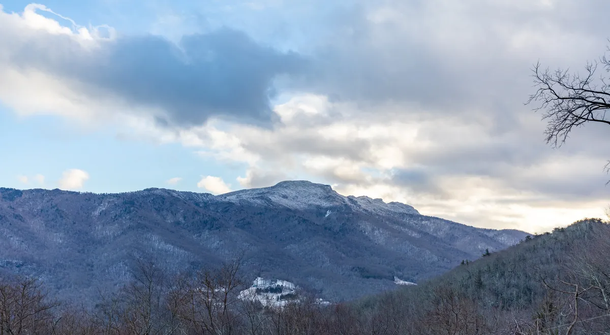 A panoramic view of snow-capped mountains beneath a cloudy sky, offering a tranquil and inspiring look at the region's scenic hiking opportunities. The rolling hills and untouched nature evoke the spirit of outdoor exploration.