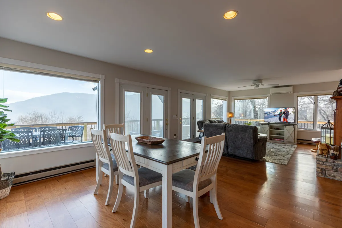 A comfortable dining area set beside large windows offers a panoramic view of the mountains. The space blends a stylish dining table with a cozy lounge area and television, inviting both shared meals and relaxed moments framed by natural beauty.