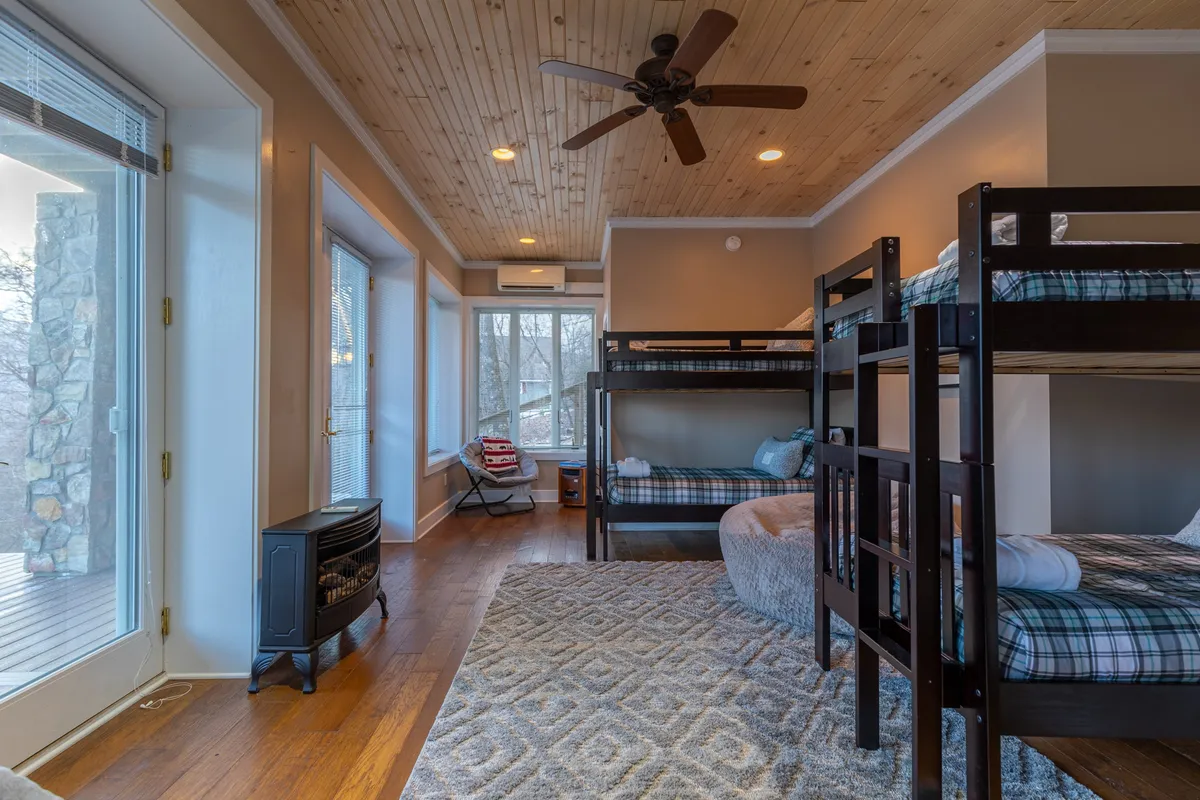 A playful and inviting bunk room with sturdy bunk beds, a cozy seating area, and large windows that let in plenty of daylight. The space is arranged to encourage both restful sleep and fun, with touches that appeal to kids and adults alike.