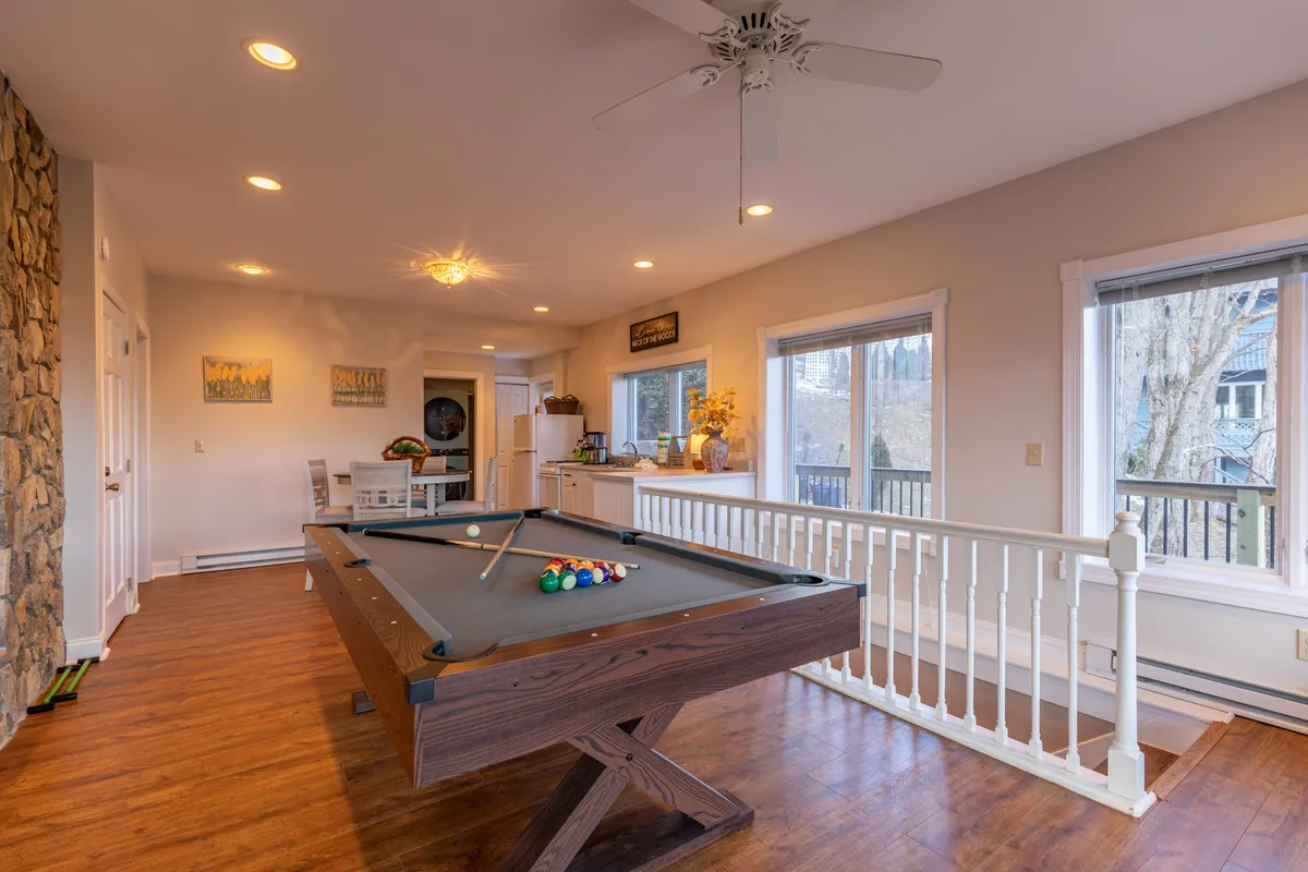 A bright, casual entertainment space highlighting a pool table, windows overlooking the outdoors, and a compact kitchenette area. The overall vibe is playful and relaxed, ideal for game nights and easy snack access.